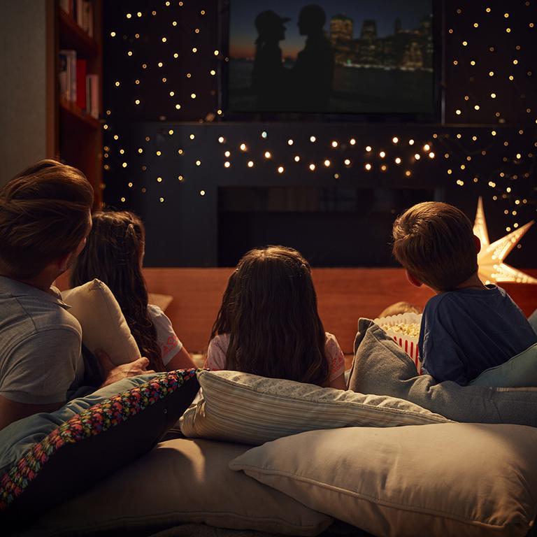 A family of 5 watching a movie at home with Christmas decorations.