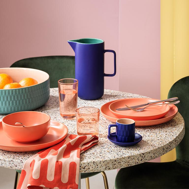 Image of a round, terrazzo table with blue and coral dinnerware.