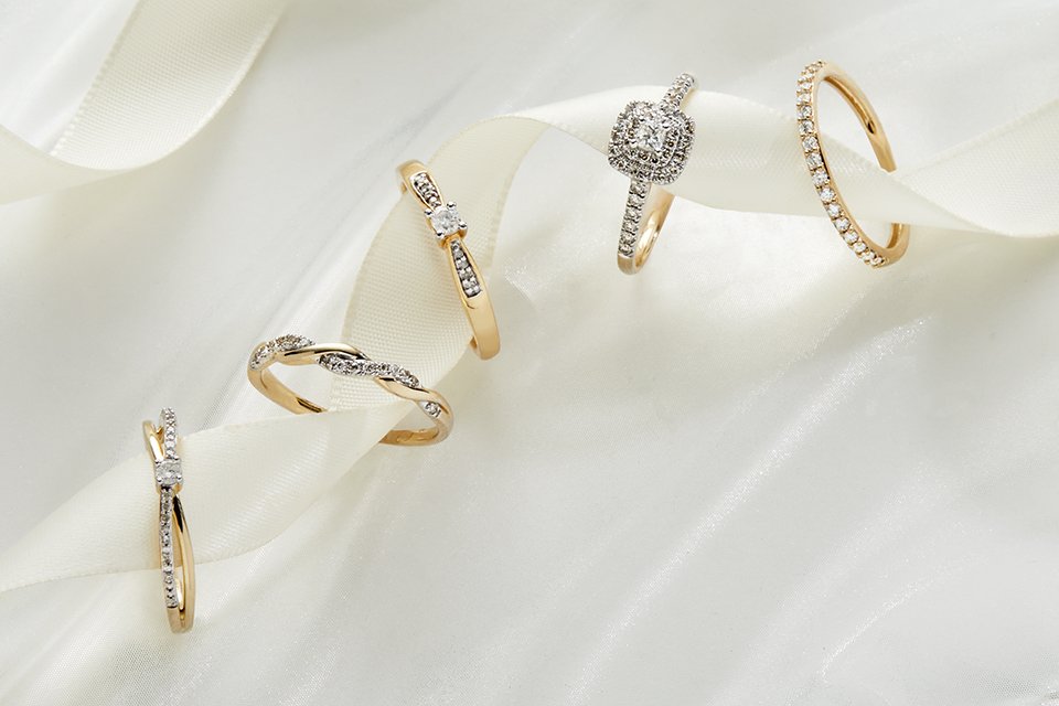 Five yellow gold rings in different styles and stones on a white ribbon.