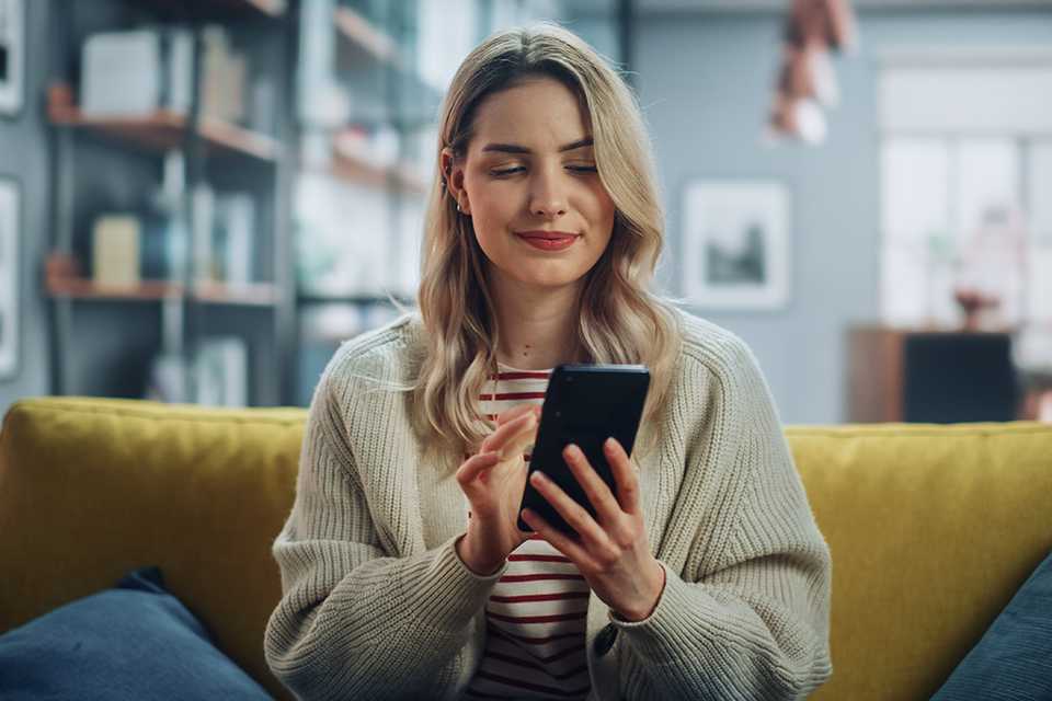 A woman sitting on a sofa looks at her mobile phone.