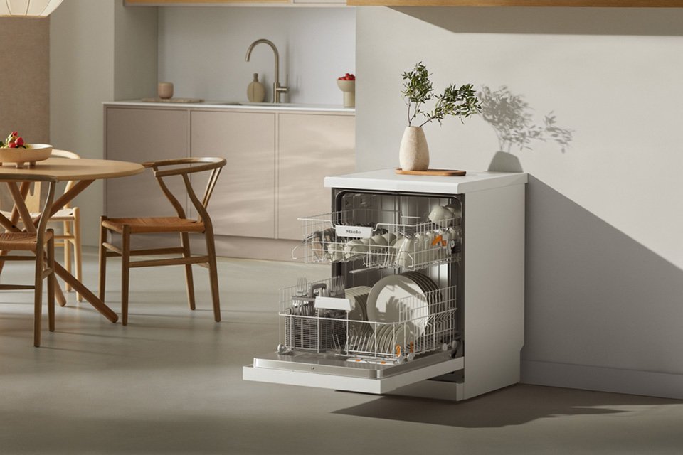 An opened Miele dishwasher loaded with plates, mugs and glasses.