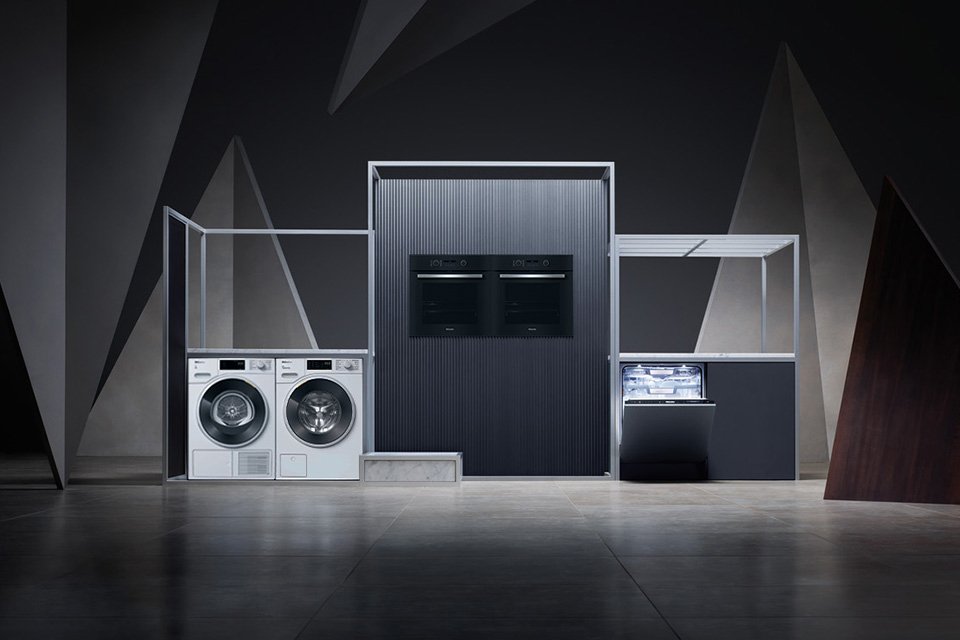 Miele's grey-toned washing machine, tumble dryer, two ovens and a dishwasher on a stage-like setup.