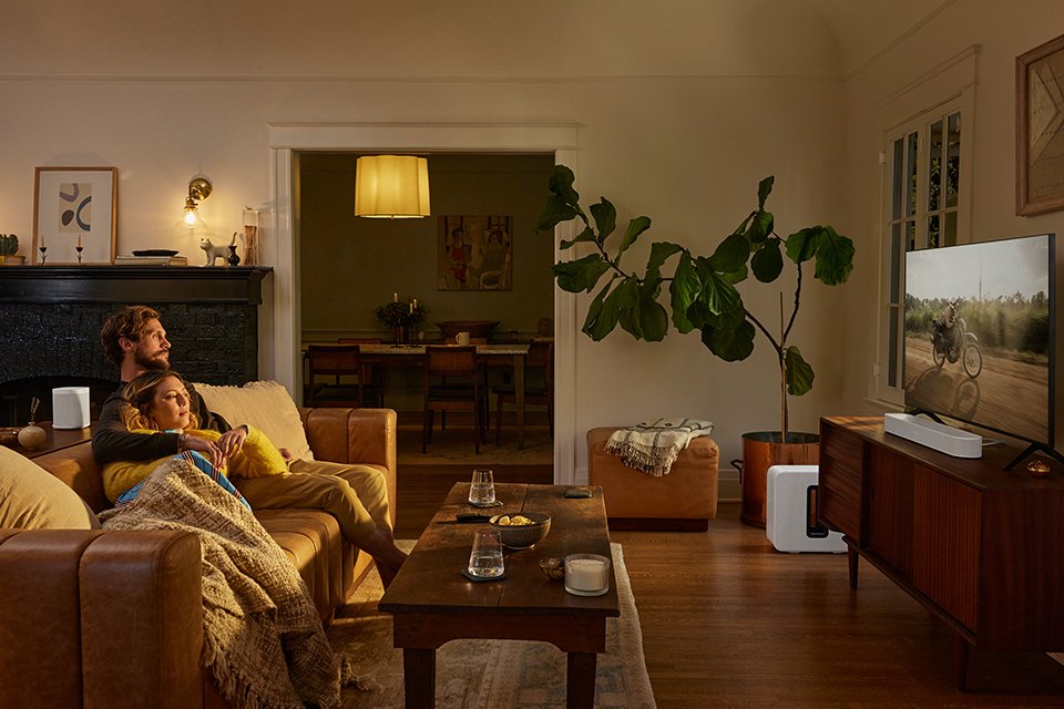 A Sonos soundbar placed under the television with a family watching it.