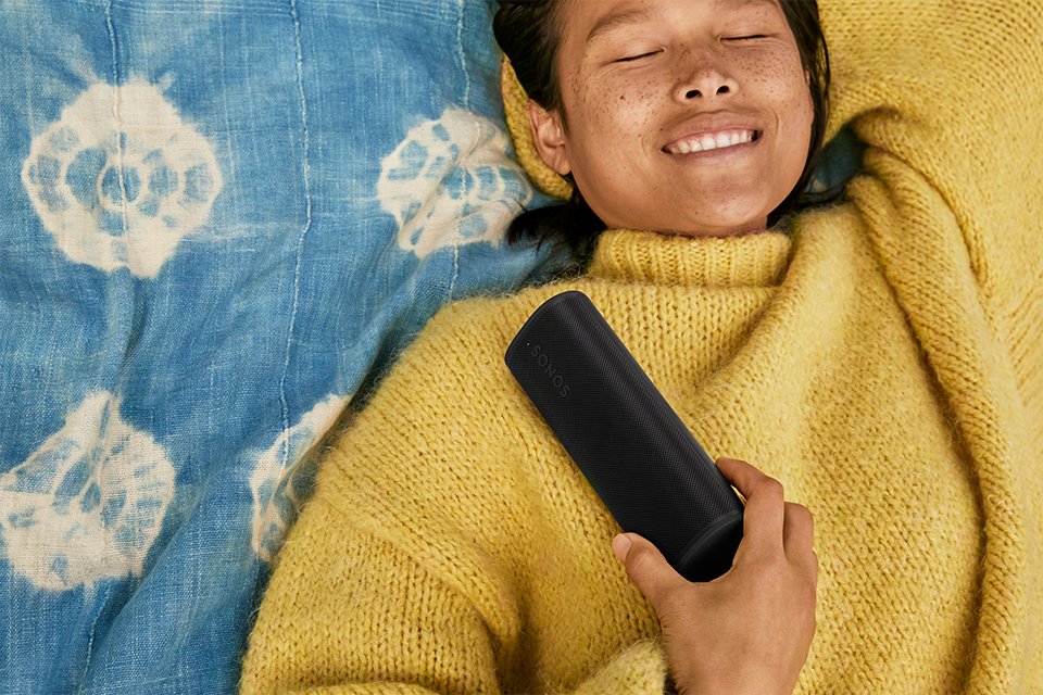 A woman smiling while listening to music on Sonos Roam 2 speaker.