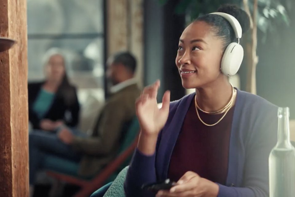 A woman listening to music on Sonos Ace headphone while being served a drink.