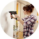 Woman drilling wall to put up a frame with photo.