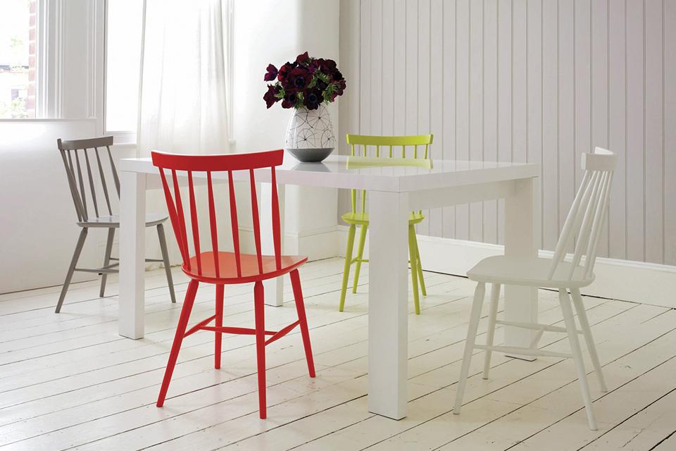 Image of a white dining set with assorted coloured chairs.