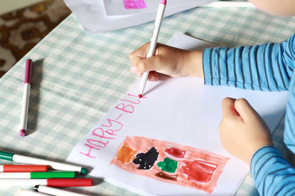 A child using colouring pen for writing a birthday card.