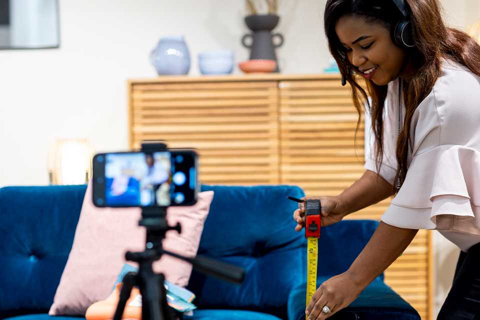 A Habitat adviser measures a blue sofa whilst on a video call.
