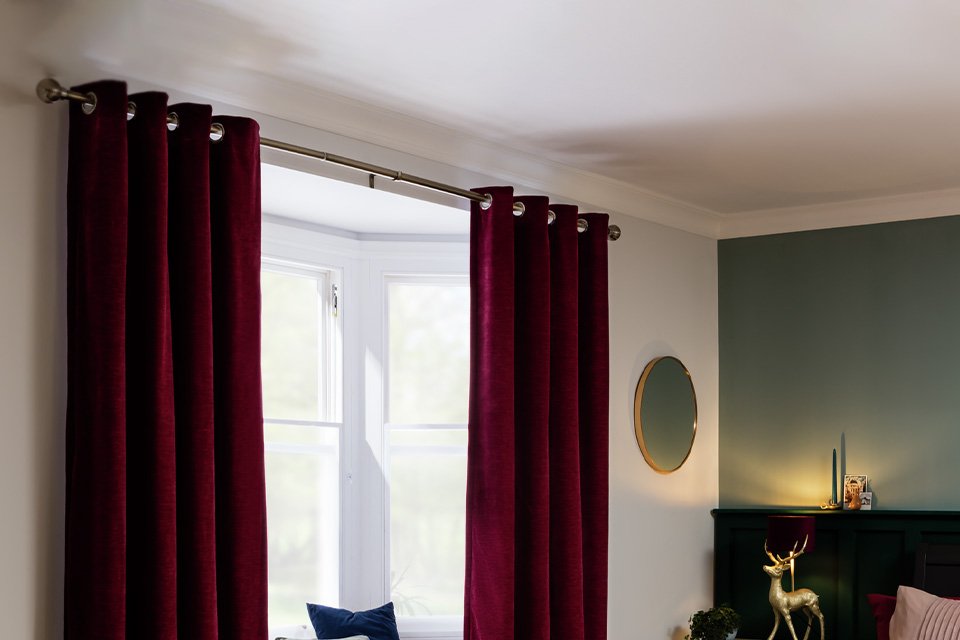 Red curtains hanging on a silver curtain pole in a living room above a bay window