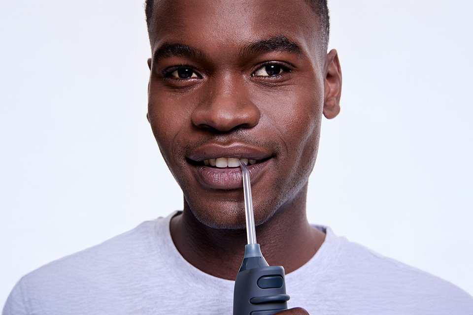 A man flossing his teeth using a graphite black Ordo Hydro Sonic+ water flosser.