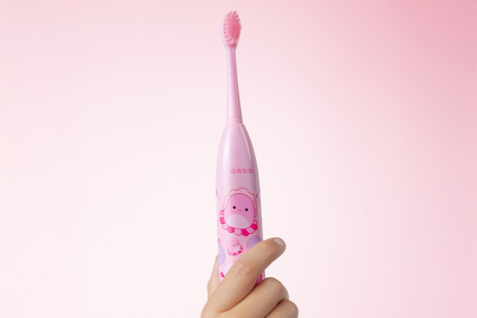 A hand holding the pink Ordo Squishmallow toothbrush up.