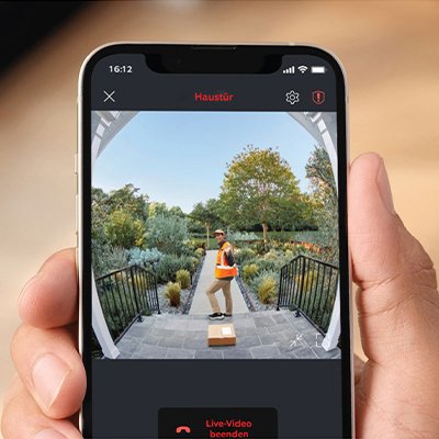 A hand holding a mobile showing the video of a delivery guy in front of the door through Ring battery video doorbell.