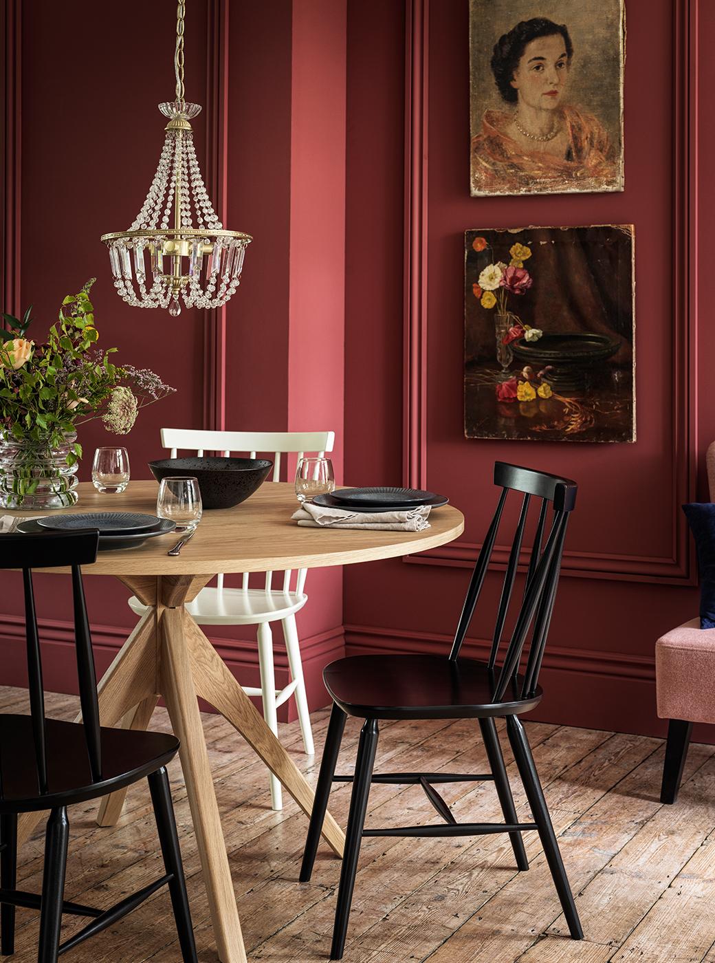 Black and cream dining chairs around light oak dining table with maroon walls in the background.