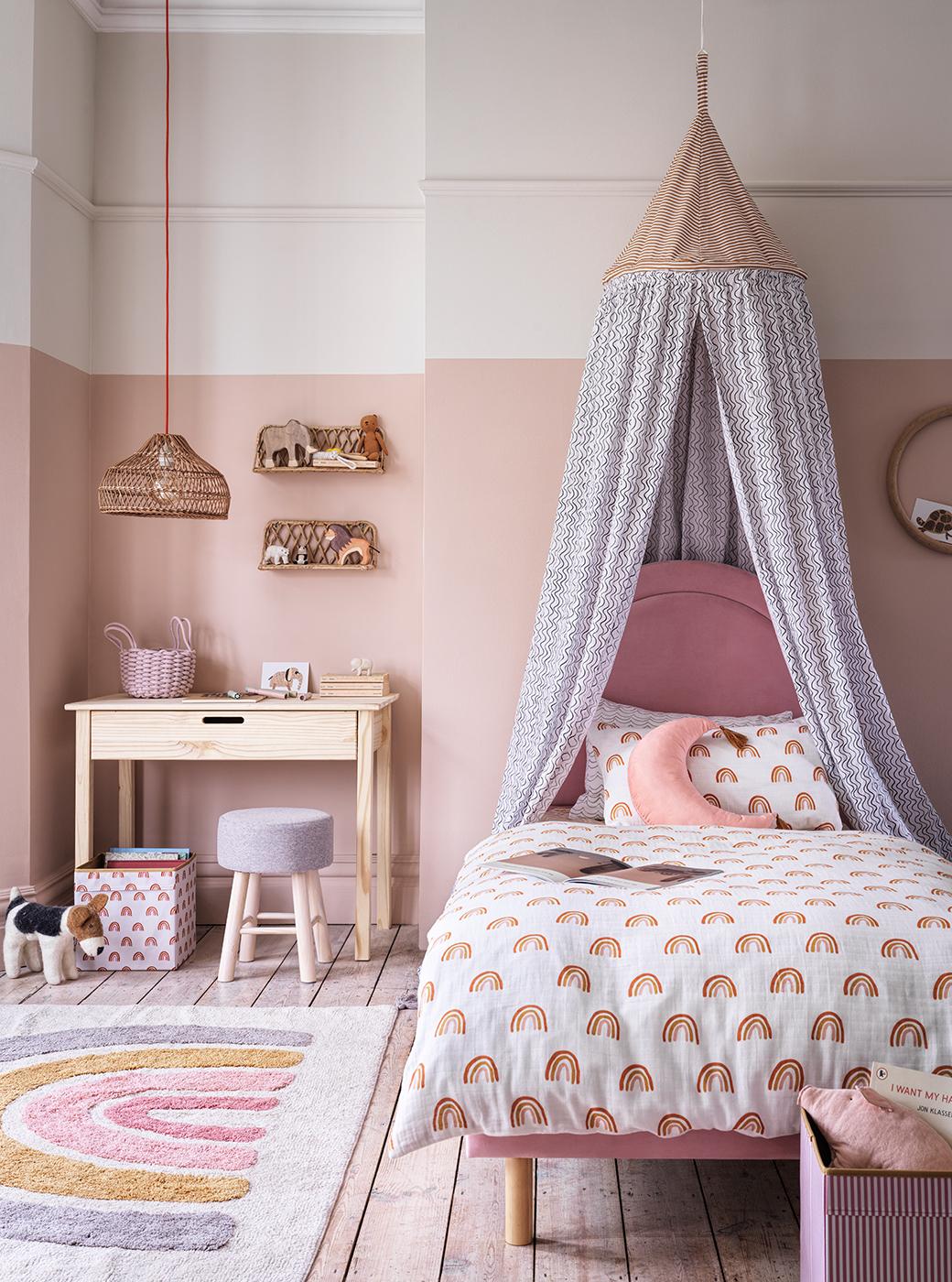 Kids bedroom with light pink walls featuring kids desk and chair and pink bed with rainbow bedding.