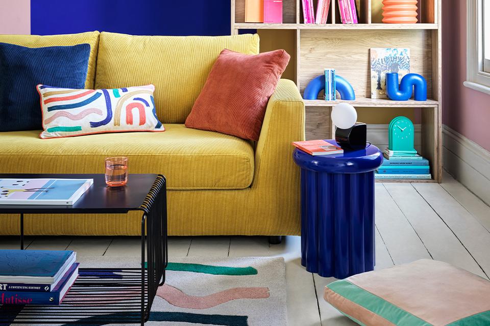 Image of yellow sofa with blue cushion and side table.