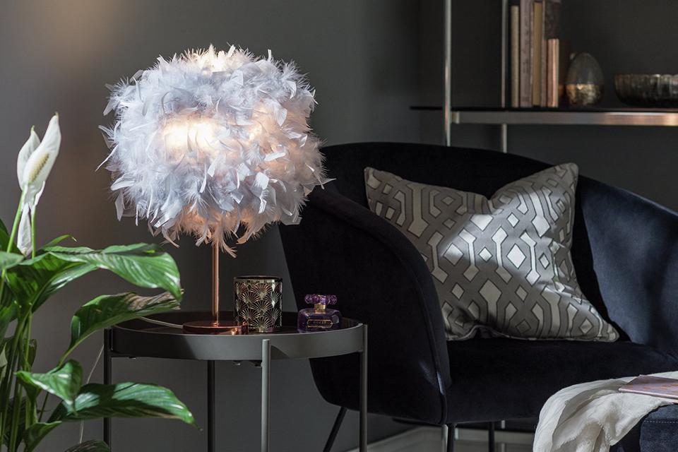 Rose gold lamp with feather shade on black side table.