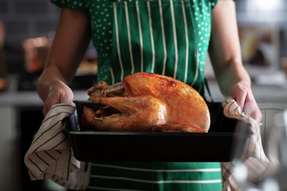 Woman holding turkey in roasting tray.