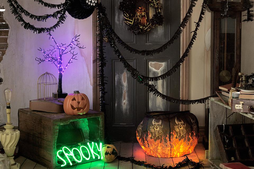 A living room decorated with a hanging long-legged spider, inflatable cauldron, light-up sign and wreath.