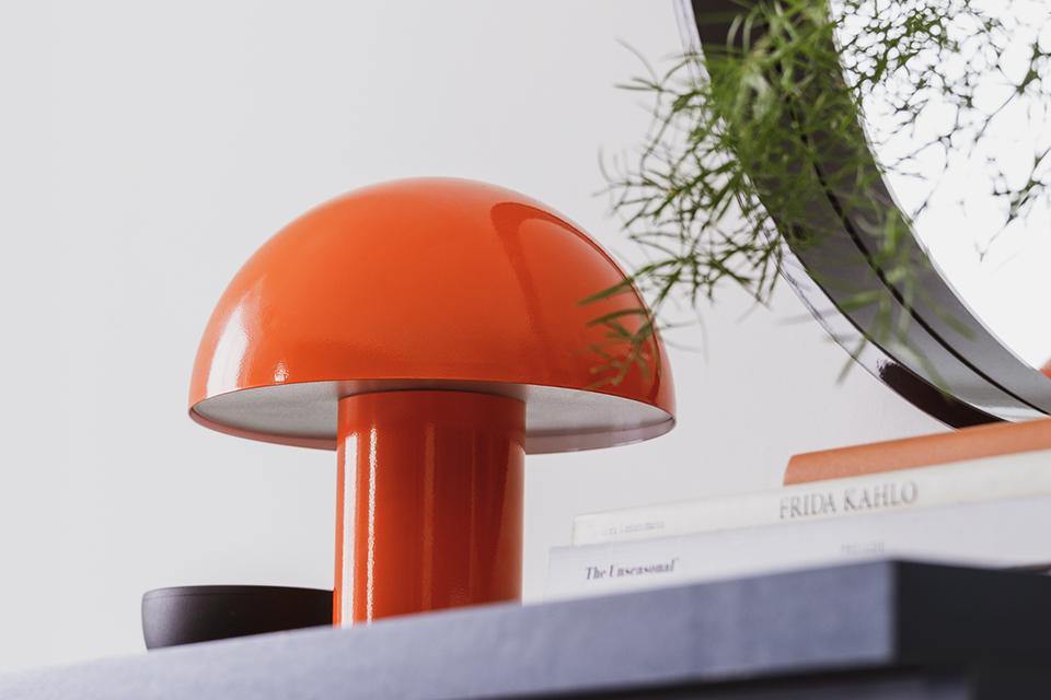 Orange mushroom lamp on shelf next to books.