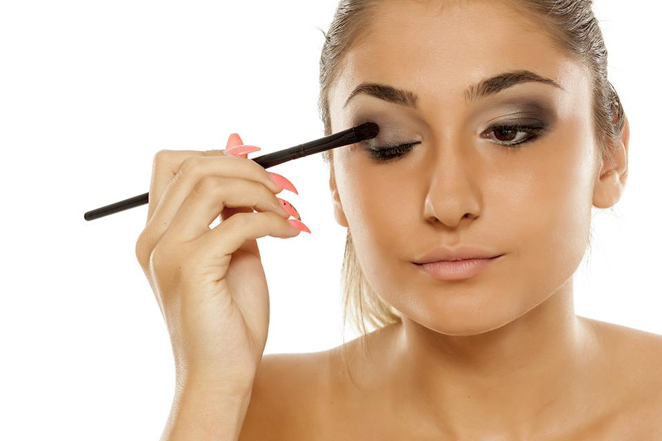 Woman applies dark grey eyeshadow to the outside of her eyelid.