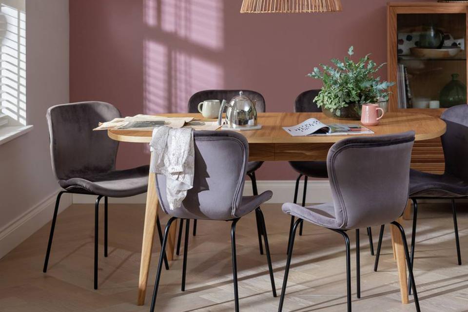 A pink and white dining room with wooden dining table and grey chairs.
