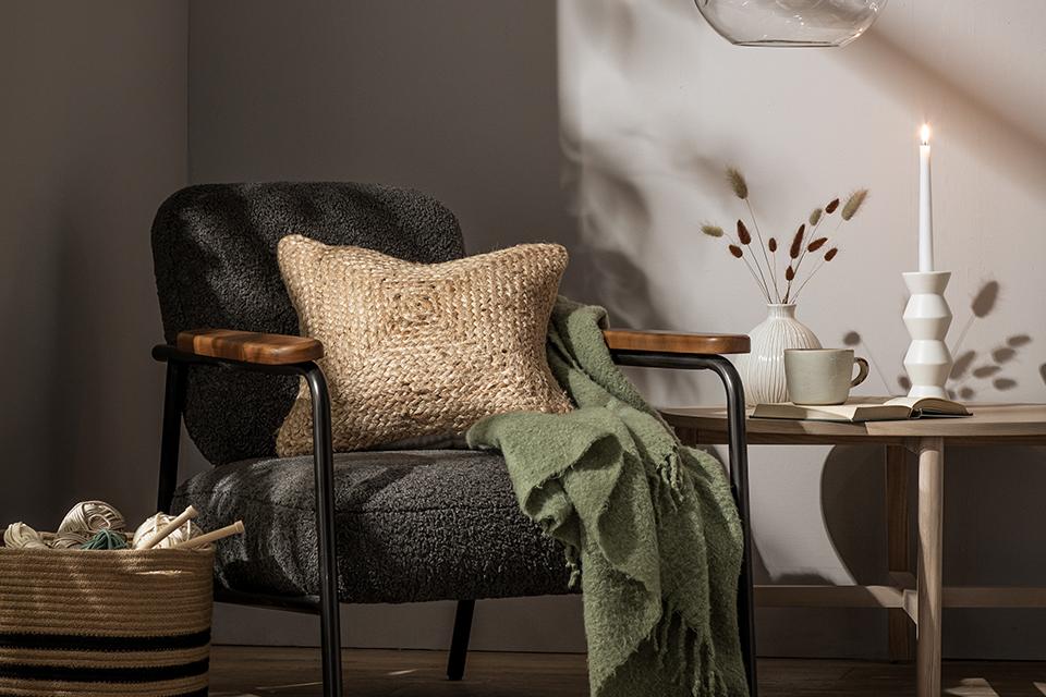 Image of a grey armchair with a jute cushion and a sage green throw.