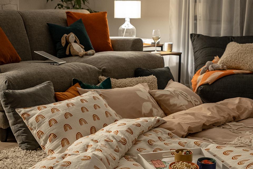 Image of a living room duvet den on the floor next to a sifa with lots of cushions and snacks.