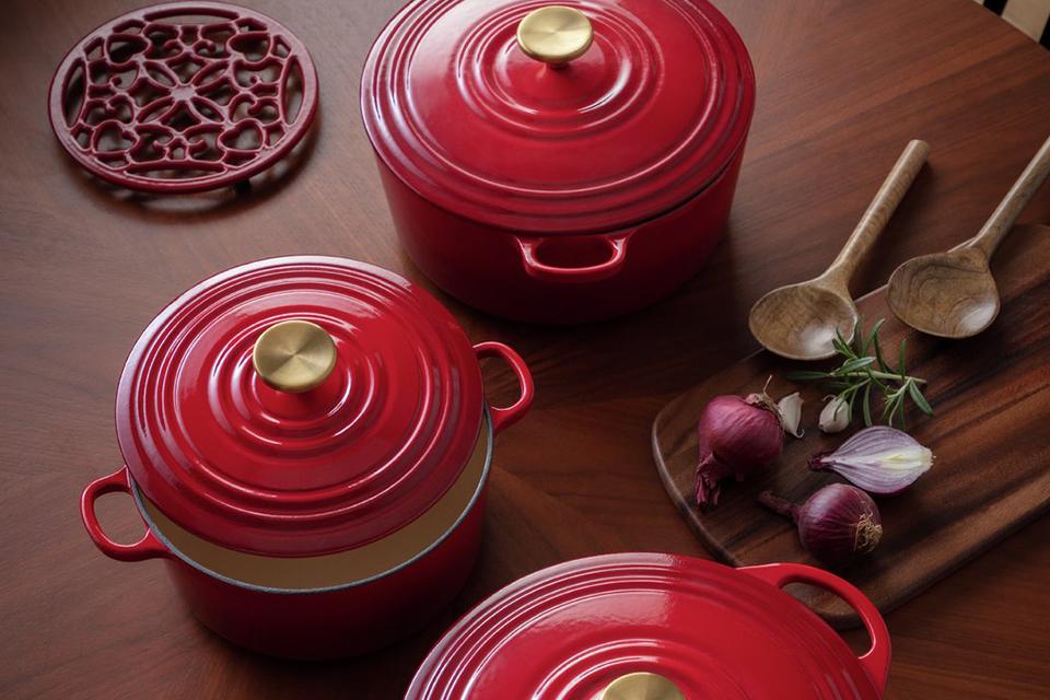 Image of 3 red cast iron pots with gold handles on a table.