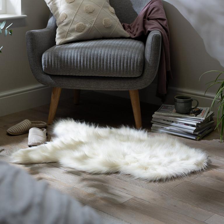 Image of cream faux sheepskin rug in front of a grey armchair.
