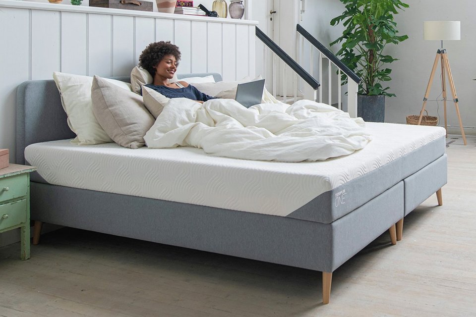 A woman using her laptop and relaxing on Tempur One Medium Memory Foam Mattress.