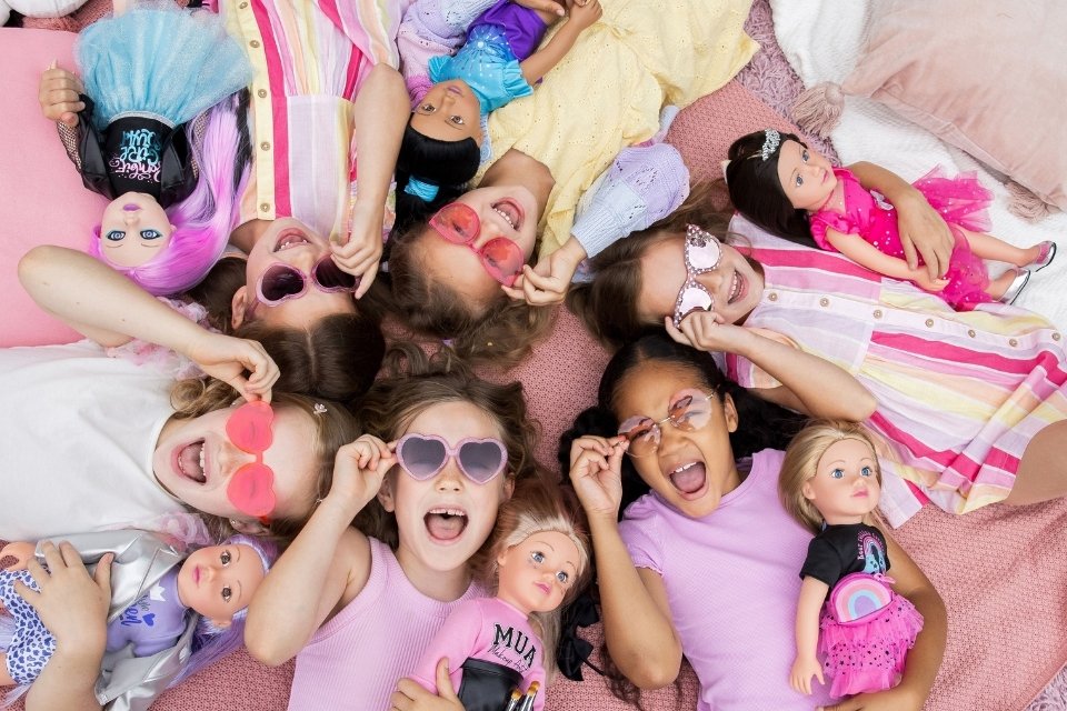 Group of girls laughing and smiling while holding their 18 inch DesignAfriend dolls, looking up at camera.