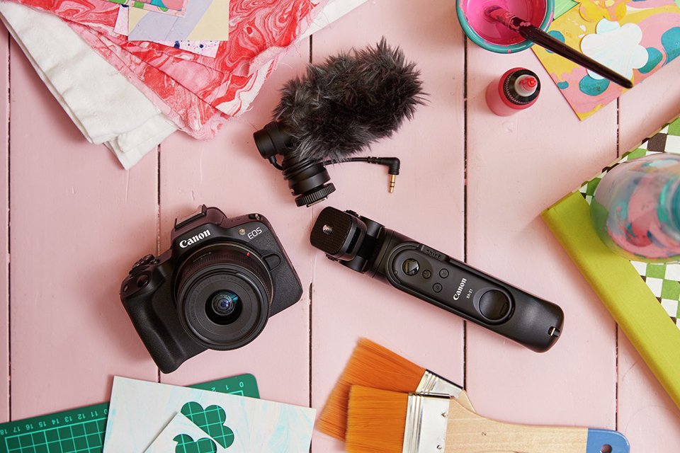 A DSLR camera along with camera accessories placed on a pink background.