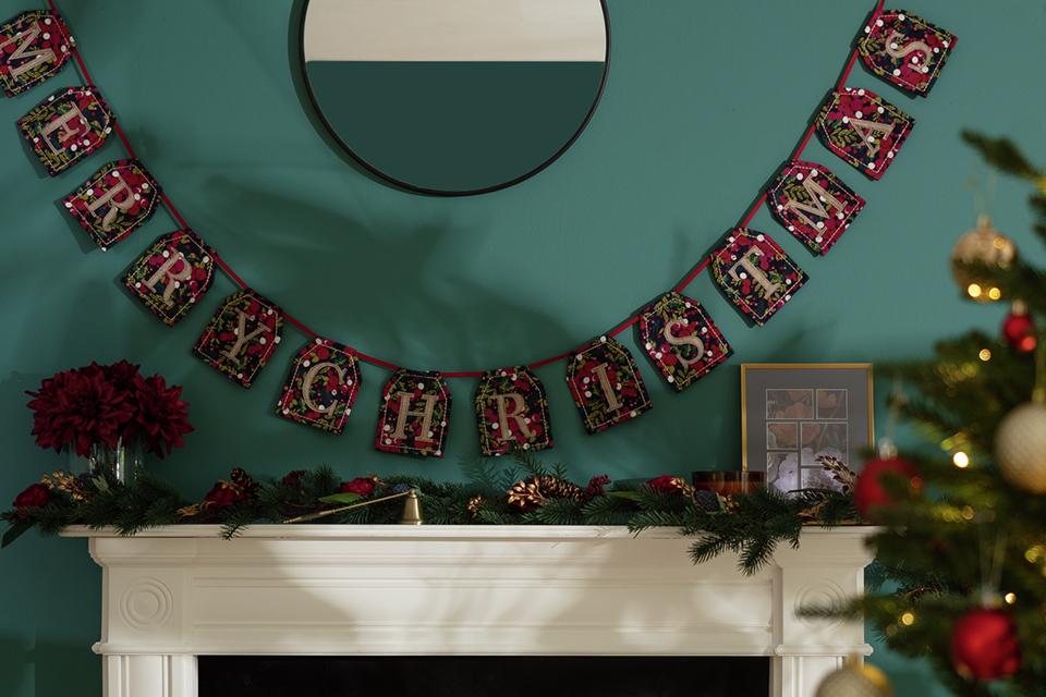 Image of a fabric garland which spells 'Merry Christma's hanging above a fireplace.