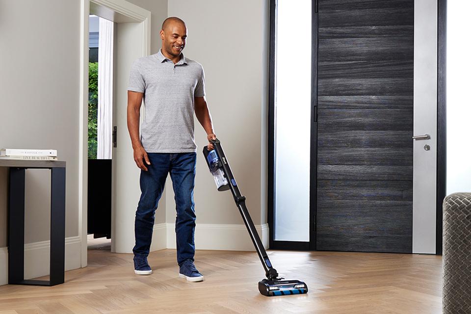 A man cleans a polished wood floor with a Shark cordless vacuum.