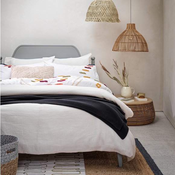 White bedding on grey bed frame with rattan hanging lamp shades.