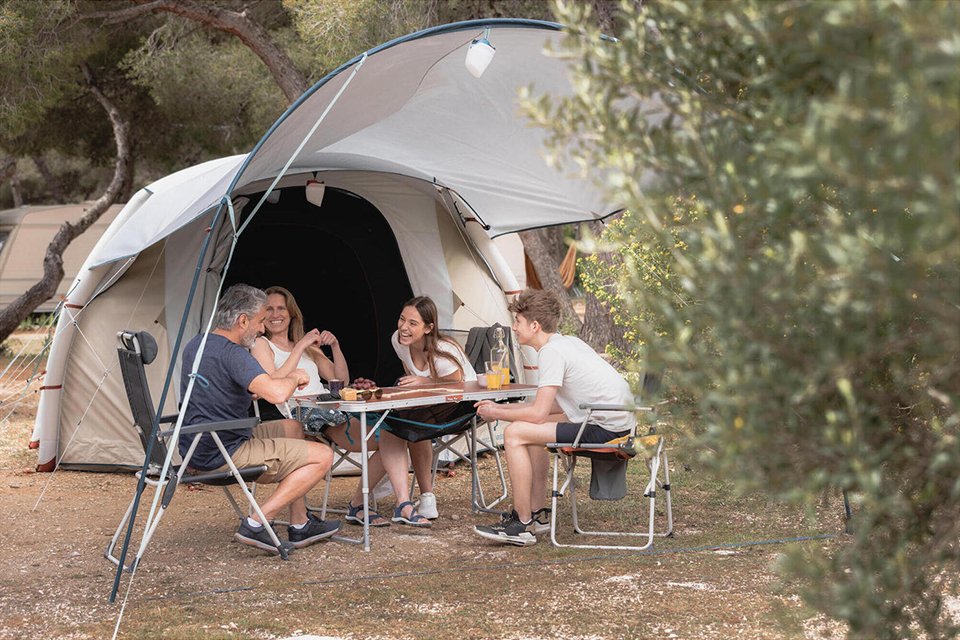 A family of 4 sitting outside their tent on a folding camping dining table set. 