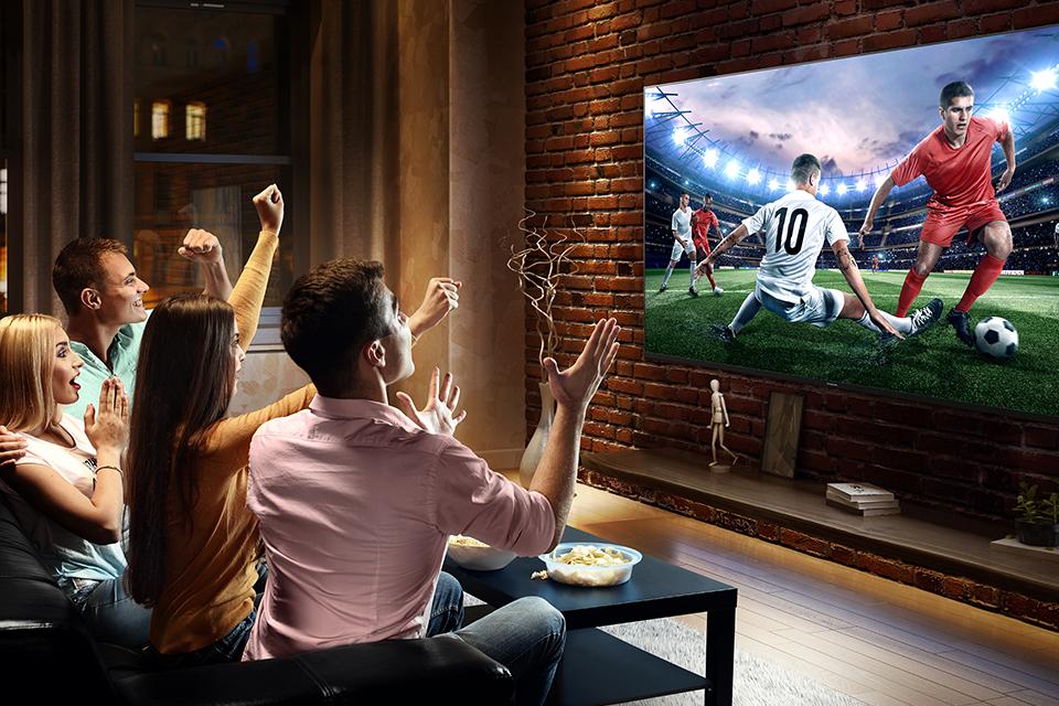 A group of friends cheer as they watch a football game on a large TV screen.