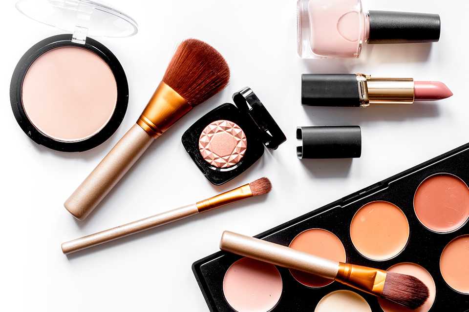 Cosmetic products including make-up, nail polish, lipstick and blush on a white background.