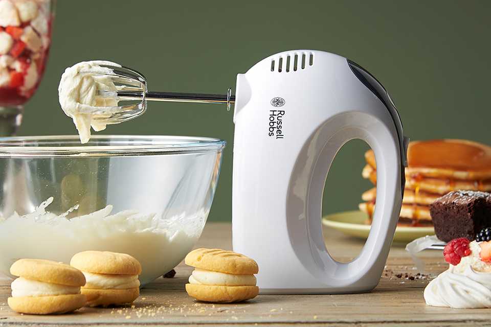 A white Russell Hobbs hand mixer placed on a kitchen countertop.