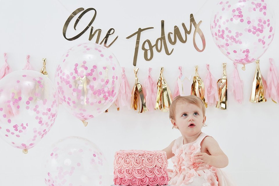A baby's first birthday party with pink and gold themed decorations.
