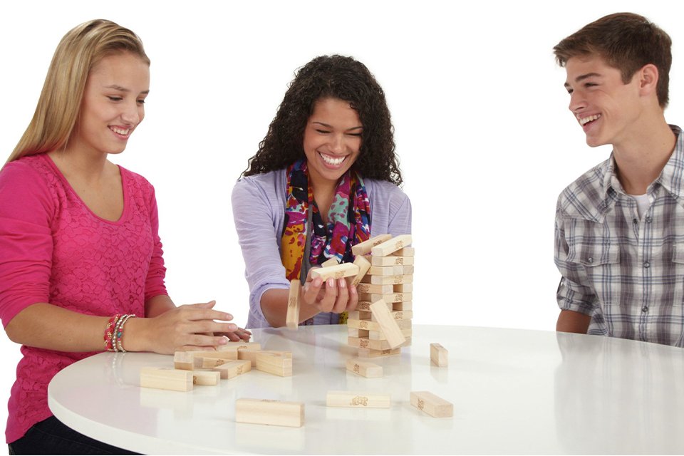 Three teenagers playing Jenga The Original Board Game from Hasbro Gaming.