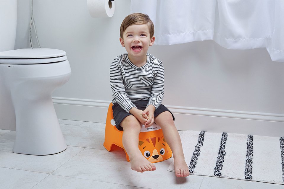 A toddler sitting on an orange baby Einstein tiger potty.