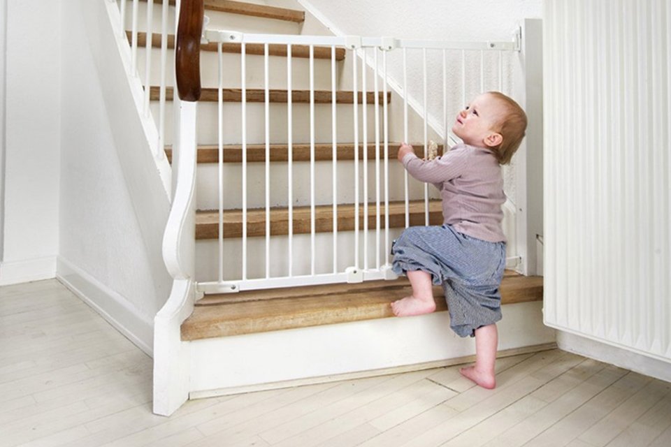 A baby trying to open the safety gate at the start of a staircase.