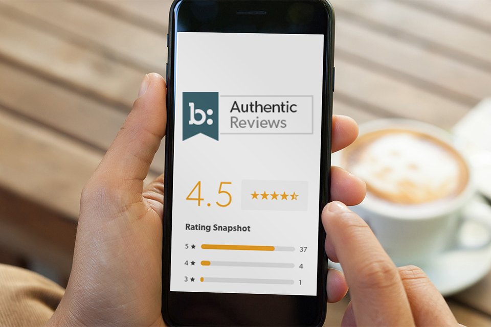 Person holding smartphone displaying 4.5-star authentic product reviews with rating breakdown, next to a cup of coffee on a wooden table.