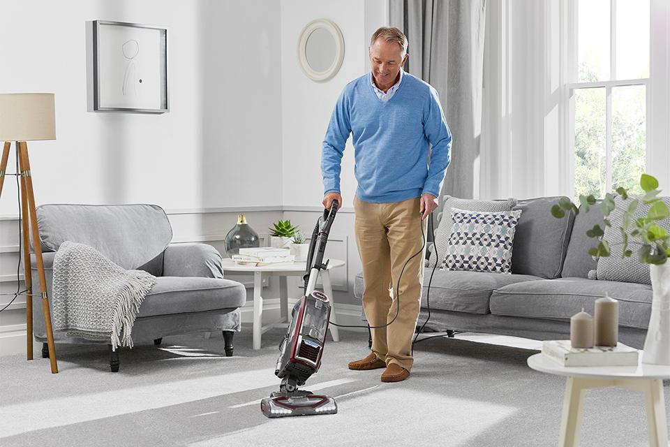 A man vacuuming the living room floor.