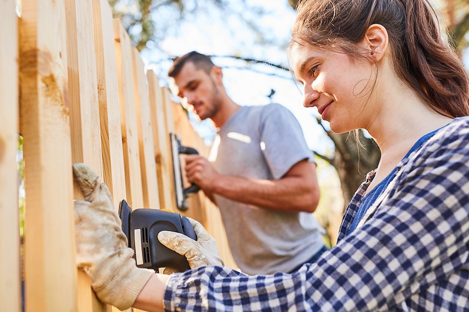 Man and woman sanding down a fence.