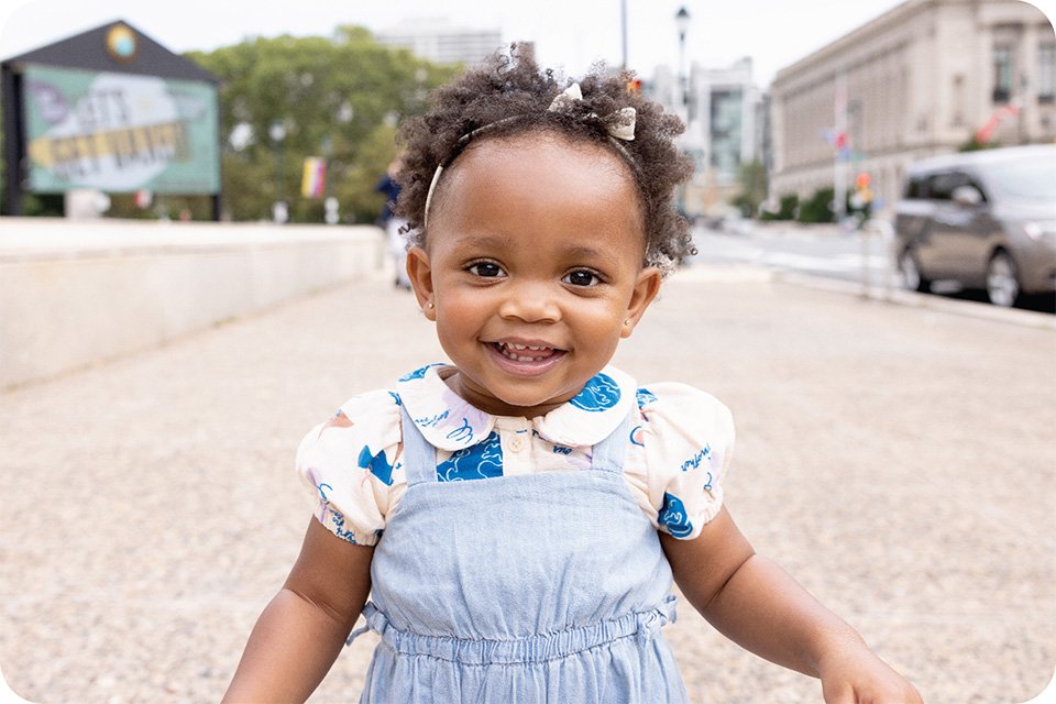 A smiling toddler walking on a pavement.
