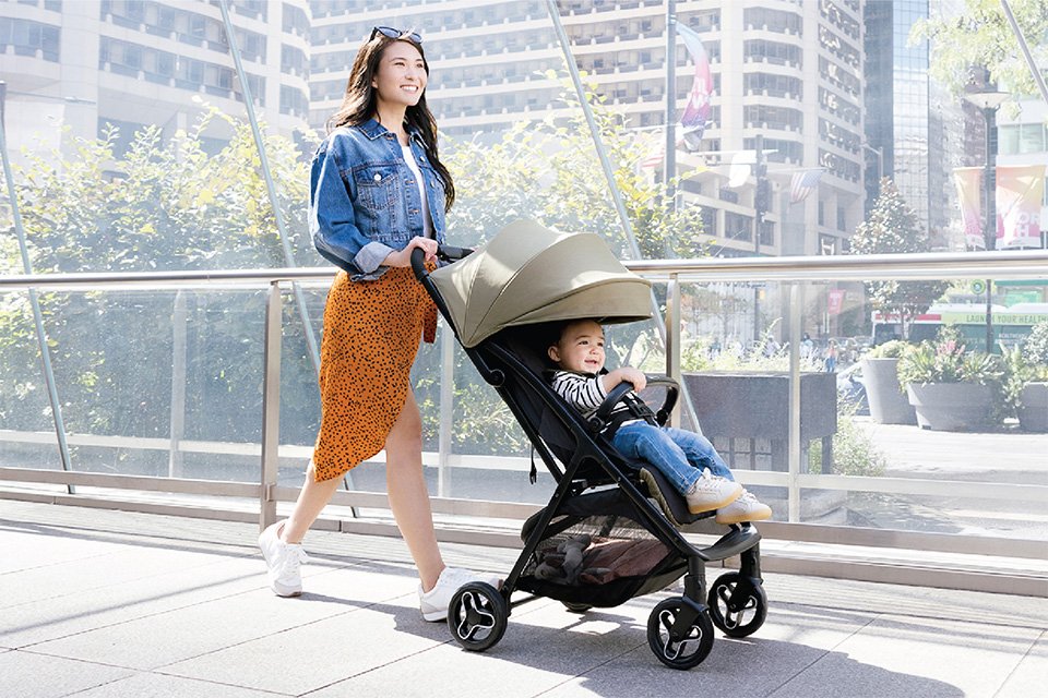 A woman walking with a baby on a travel stroller.
