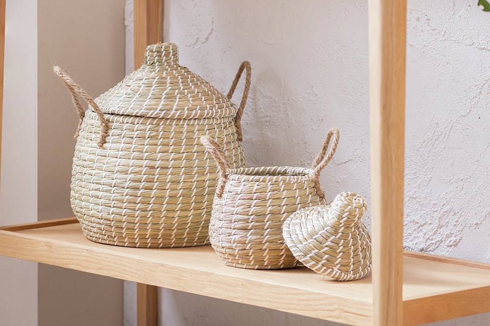 Habitat Pack of 2 Seagrass Lidded Round Basket in natural finish placed on a wooden storage rack.